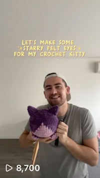 a man is holding up a crochet kitty