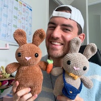 a man holding up two crocheted bunnies